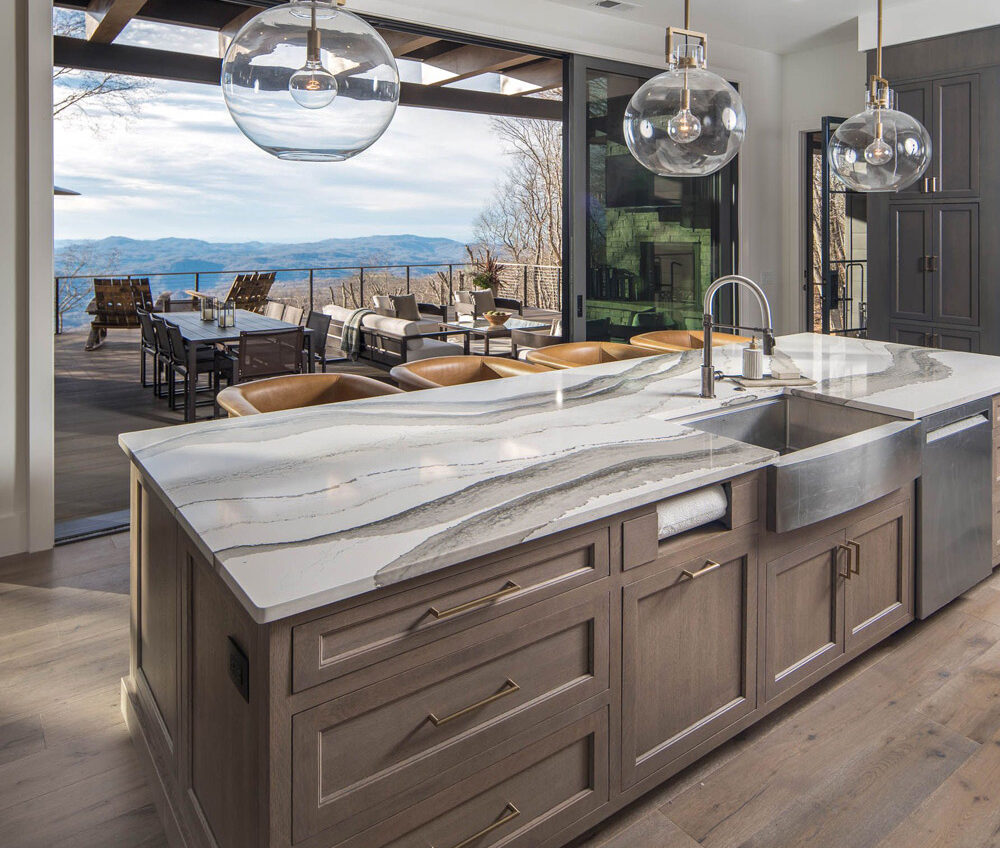 Kitchen island with sink overlooking back deck with outdoor dining and mountain view.