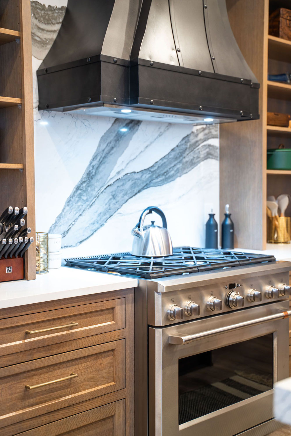 Kitchen gas top oven range with marble backsplash and custom hood and cabinetry.